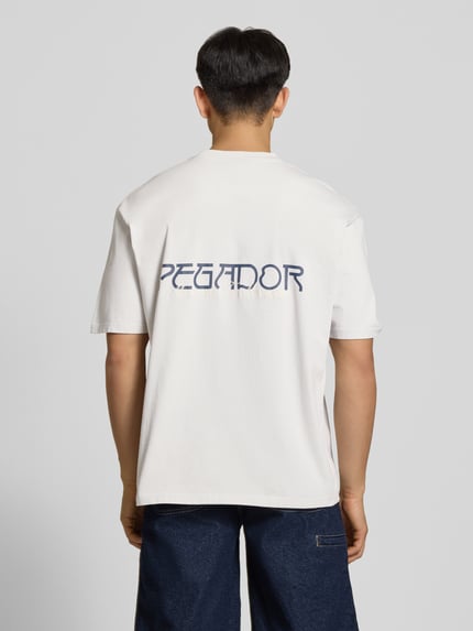 Männermodel trägt Oversized T-Shirt mit 1/2-Arm Modell 'Zernez' von Pegador, Reine Baumwolle, Rundhalsausschnitt, Label-Detail, Rückenlänge 72 cm, Ganzkörperansicht Rückansicht.