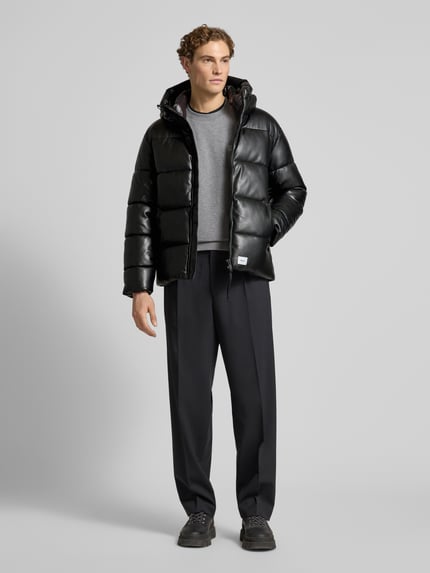 Männermodel trägt Regular Fit Steppjacke mit Logo-Patch Modell 'Coen' von khujo in schwarzer Stepp-Optik mit Reißverschluss, Kapuze mit Tunnelzug und gefüttertem Stehkragen, Ganzkörperansicht von vorne.