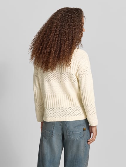 Frauenmodel trägt Boxy Fit Strickpullover aus reiner Baumwolle Modell 'ALAYA' von Pepe Jeans, Strickoptik, Struktur, Rundhals, Langarm, Seitenschlitze, asymmetrisch, Ganzkörperansicht Rückansicht.