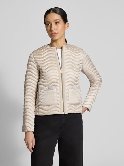 Modelka nosi Slim Fit Steppjacke mit aufgesetzten Taschen Modell 'Tamina' od SAVE THE DUCK, krój slim fit, jasny beż, faktura pikowana, zapięcie na zamek, okrągły dekolt, długość tyłu w rozmiarze S: 55 cm, szerokość ramion w rozmiarze S: 38 cm, szerokość klatki piersiowej w rozmiarze S: 47 cm, długość rękawa w rozmiarze S: 62 cm, widok całej sylwetki z przodu.