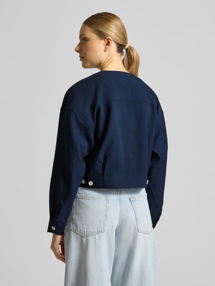 Männermodel trägt Boxy Fit Kurzblazer aus Viskose-Mix von Tommy Hilfiger, efekt: jednolity kolor, pudełkowy krój, okrągły dekolt, długość: krój krótki, wyhaftowane logo, listwa guzikowa z 1 guzikiem, długi rękaw, mankiet, kieszenie na piersi, materiał: mieszanka wiskozy, Ganzkörperansicht Rückansicht.