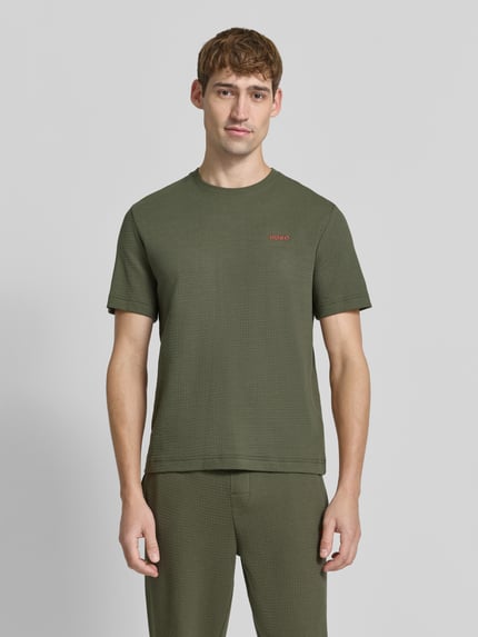 Männermodel trägt Regular Fit T-Shirt aus Baumwoll-Mix von HUGO in Olivgrün mit feiner Struktur, Ganzkörperansicht von vorne.
