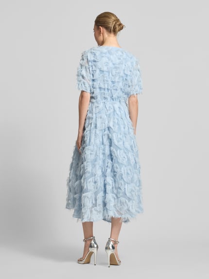 Frauenmodel trägt Cocktailkleid mit Fransen Modell 'PAZYLLA' von YAS in hellblau, A-Linie, strukturierte Oberfläche, Ganzkörperansicht Rückansicht.