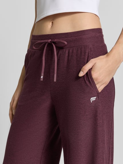 Frauenmodel trägt Wide Fit Sweatpants mit Label-Detail Modell 'CLOUD' von Fabletics in meliertem Dunkelrot, weiche Textur, elastischer Bund mit Tunnelzug, elastischer Material-Mix, Nahaufnahme Oberkörper, Kontext: Damen Sweatpants, Innenbeinlänge bei Größe S 75 cm.
