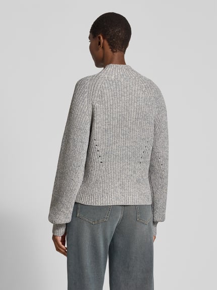 Frauenmodel trägt Pullover mit markantem Zopfmuster Modell 'Frescienne' von BOSS in Melange-Optik, Strickstruktur, Ganzkörperansicht Rückansicht.