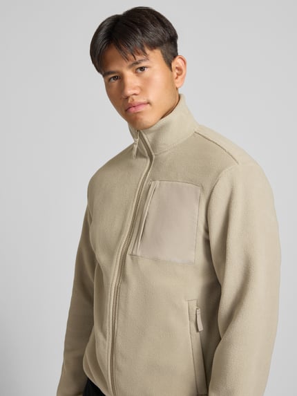 Männermodel trägt Fleecejacke mit Zweiwege-Reißverschluss Modell 'MASON' von JACK & JONES in Beige mit Stehkragen, Nahaufnahme Oberkörper.