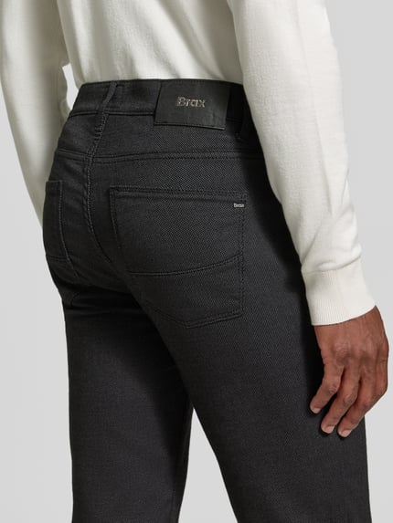 Männermodel trägt Stoffhose aus Baumwoll-Mix mit Viskose-Anteil Modell 'Cadiz' von Brax in Melange-Optik, 5-Pocket-Design, Detailaufnahme Rückansicht.