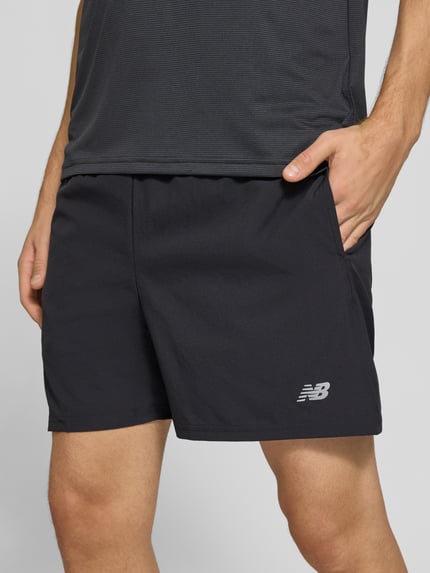 Männermodel trägt Shorts mit elastischem Bund und Logo von New Balance, schwarz, Regular Fit, Nahaufnahme Oberschenkel, Kontext: Innenhose, Bundweite 40 cm, Innenbeinlänge 13 cm