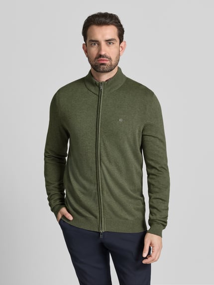 Męski model nosi Strickjacke mit Reißverschluss od Christian Berg Men, oliwkowa bawełna organiczna, stegnany dół, zamek, widok z przodu, ujęcie całej sylwetki.