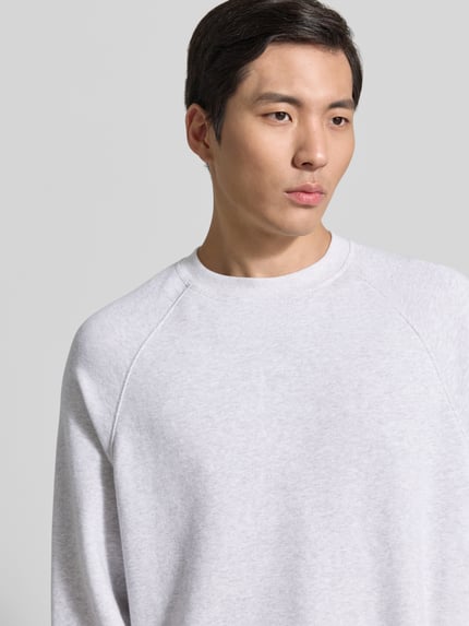 Männermodel trägt Sweatshirt mit Rundhalsausschnitt Modell 'ATUBAY' von American Vintage aus Baumwoll-Elasthan-Mix in Hellgrau, Nahaufnahme Oberkörper. Relaxed-Fit, Rückenlänge 67 cm, Ärmellänge 77 cm, Größe M/L.