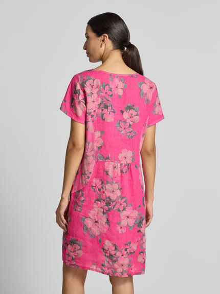 Frauenmodel trägt Leinenkleid in Minilänge Modell 'Miraa' von ZABAIONE in leuchtendem Pink mit floralem Muster, Rückenansicht, Ganzkörperansicht. Leicht taillierte Passform, elastischer Leinen-Baumwoll-Mix, kurzärmlig, Rundhalsausschnitt, Länge bei Größe S ca. 81 cm, weich strukturierte Oberfläche.