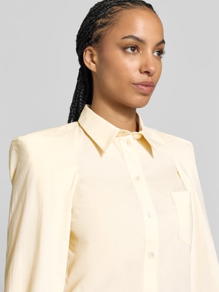Frauenmodel trägt Hemdbluse aus Baumwoll-Mix von Iro in hellem Gelb, glatte Textur, Hemdblusenkragen, Knopfleiste, Nahaufnahme Oberkörper.