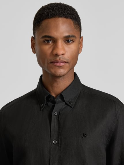 Męski model nosi Regular Fit Freizeithemd aus reinem Leinen Modell 'LIAM' von BOSS, jednokolorowy, kołnierzyk typu button down, wyhaftowane logo, listwa guzikowa na całej długości, długi rękaw, mankiet, wykończenie: cieniowana przędza, materiał: len; nahaufnahme górnej części ciała.