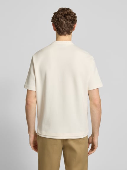 Mężczyzna model nosi T-Shirt mit Logo und Rundhalsausschnitt od ARMANI EXCHANGE, biała bawełna, krój regular fit, widok całej sylwetki od tyłu.