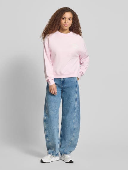 Frauenmodel trägt Boxy Fit Sweatshirt aus reiner Baumwolle von Tommy Jeans, Optik: Unifarben, Label-Print, Crew Neck, Langarm, gerippter Abschluss, Materialverarbeitung: Sweat, Farbe: Hellrosa, Ganzkörperansicht von vorne.