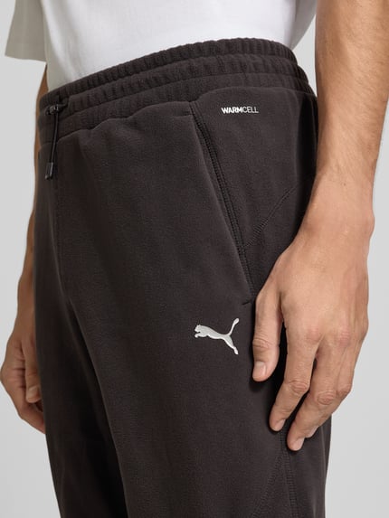 Männermodel trägt Relaxed Fit Sweathose mit Logo-Print Modell 'PUMATECH' von PUMA Performance, Schwarz, Nahaufnahme Hüfte und Hand.