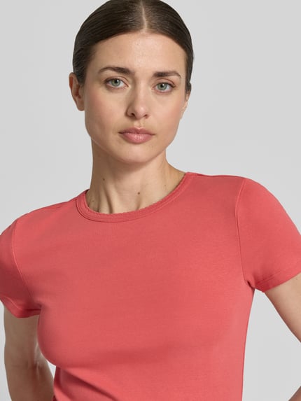 Vrouwenmodel draagt T-Shirt met Feinripp en Rundhalsausschnitt van Jake*s Casual in koraalroze, slim fit, katoenmix, detailopname bovenlichaam.