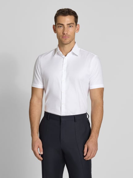 Męski model nosi Slim Fit Business-Hemd aus Baumwolle mit Kentkragen od Jake*s, biała bawełna, krój slim fit, kołnierz kent, listwa guzikowa, długość pleców w rozmiarze 39/40: 78 cm, szerokość w rozmiarze 39/40: 47 cm, długość rękawa w rozmiarze 39/40: 24 cm, pełny widok z przodu.