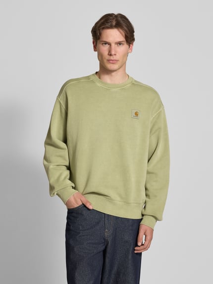 Mannelijk model draagt heren sweatshirt van puur katoen in relaxed fit, model 'Nelson' met labeldetail van Carhartt Work In Progress, ronde hals, ruglengte maat M 68 cm, mouwlengte maat M 63 cm, lichtgroene kleur, rechte vormen, gladde textuur. Ganzkörperansicht von vorne.