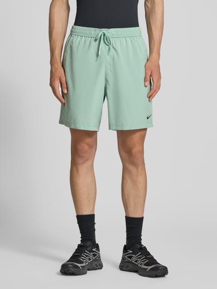Männermodel trägt Shorts mit Logo-Print und Eingrifftaschen von NIKE TRAINING in Hellgrün, Gerader-Schnitt, Kordelzug, Ganzkörperansicht von vorne. Bundweite bei Größe M: 41 cm, Innenbeinlänge bei Größe M: 19 cm.