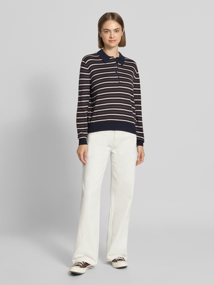 Kobiece modelka nosi koszulkę polo 'Poloshirt mit geripptem Saum' od REVIEW, mieszanka materiałów z bawełną, prosty krój, długi rękaw, kołnierzyk polo, prążkowany dół, długość tyłu w rozmiarze S: 57 cm, długość rękawów w rozmiarze S: 62 cm, kolor granatowy z paskami, białe szerokie spodnie, jasne tło, pełny widok z przodu.