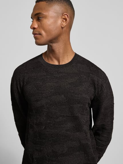 Männermodel trägt Strickpullover mit gerippten Abschlüssen von ARMANI EXCHANGE, dunkler Farbton, Material-Mix mit Baumwoll-Anteil, Nahaufnahme Oberkörper.
