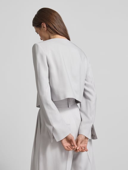 Frauenmodel trägt Asymmetrisch geschnittener cropped Blazer-curated by Vicky Heiler von SIC in hellem Viskose-Elasthan-Mix, fließende Textur, Knopfverschluss, Rückansicht, Ganzkörperansicht