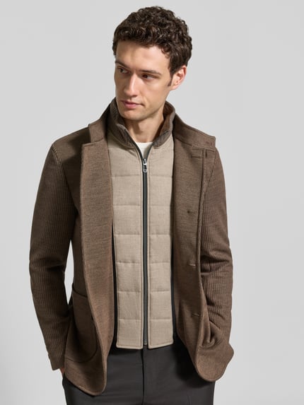 Männermodel trägt Slim Fit Sakko mit Woll-Anteil Modell 'Hypetar' von JOOP! COLLECTION in Braun, kombiniert mit heller Steppweste, Ganzkörperansicht von vorne.
