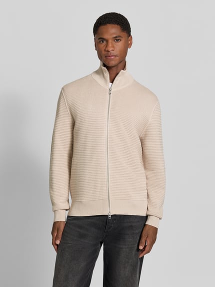 Männermodel trägt cremefarbene Regular Fit Strickjacke aus reiner Baumwolle von Marc O'Polo, feine Struktur, Ganzkörperansicht von vorne, Herren Pullover von Marc O'Polo.