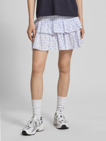 Frauenmodel trägt Ausgestellter Mini-Rock mit Volants Modell 'ZOEY' von Only, Optik: Allover-Muster, Regular-Fit, Mini-Länge, florales Muster, gesmokter Bundabschluss, Material: reine Baumwolle; Weiß- und Blautöne, glatte Textur, Ganzkörperansicht von vorne.