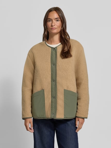 Frauenmodel trägt Wendejacke mit Rundhalsausschnitt von camel active w kolorze beżowym i zielonym, nakładane kieszenie, krój regular fit, listwa guzikowa, długość tyłu w rozmiarze 36: 68 cm, szerokość ramion w rozmiarze 36: 51 cm, szerokość klatki piersiowej w rozmiarze 36: 59 cm, długość rękawów w rozmiarze 36: 59 cm, faktura miękka i pikowana, widok całej sylwetki z przodu