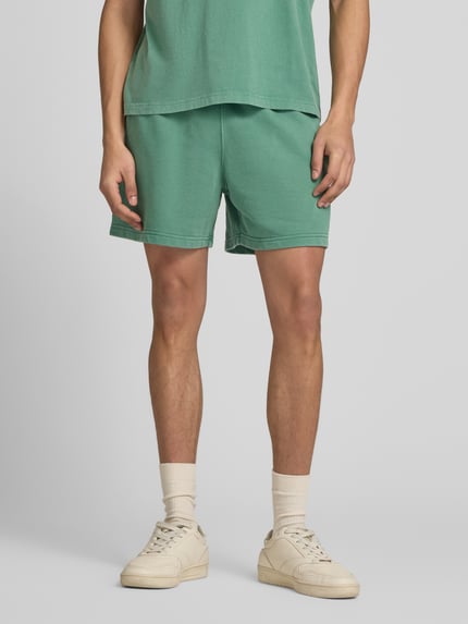 Männermodel trägt grüne Sweatshorts mit Eingrifftaschen von CHAMPION, Baumwoll-Mix, regular fit, Nahaufnahme Oberkörper bis Knie.