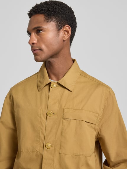 Männermodel trägt Regular Fit Freizeithemd aus reiner Baumwolle von Barbour in hellem Braun, glatte Oberfläche, Nahaufnahme Oberkörper.