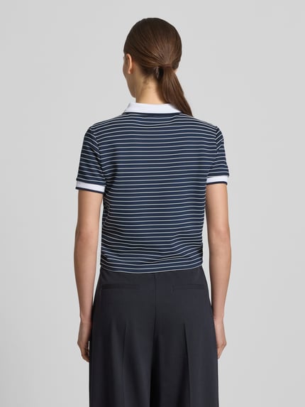 Vrouwenmodel draagt cropped poloshirt uit viscosemix model 'ALPHONSINE' van Guess met streepmotief, knoopsluiting, ruglengte maat S 49 cm. Ganzkörperansicht Rückansicht.