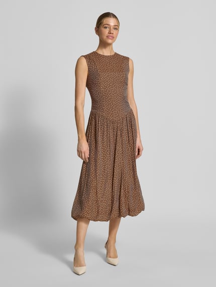 Modelka kobieca nosi Bubble Kleid mit Rundhalsausschnitt Modell 'KRISSI' od YAS, materiał z domieszką lyocellu, krój taliowany, sukienka midi, okrągły dekolt, suwak z tyłu, długość pleców w rozmiarze 36: 45 cm, szerokość w rozmiarze 36: 43 cm, brązowo-biały wzór, delikatna faktura tkaniny, widok całej sylwetki z przodu.