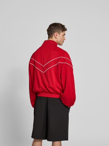 Männermodel trägt rode Bomberjacke mit raglanmouwen, witte sierstrepen, los model van RHUDE, ruglengte maat M 61 cm, schouderbreedte 49 cm, mouwlengte 67 cm, tweewegritssluiting, ritszakken, opstaande kraag; ganzlichaamsaanzicht rugaanzicht