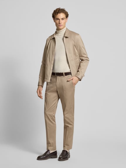 Männermodel trägt Stoffhose mit Gesäßtaschen Modell 'Tenuta' von Tiger Of Sweden, Baumwoll-Elasthan-Mix, beige, gerader Schnitt, Ganzkörperansicht von vorne.