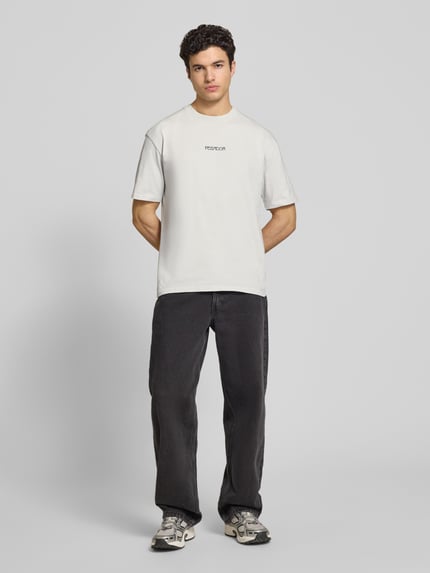Męski model nosi Oversized T-Shirt aus Baumwolle Modell 'Stavoren' od Pegador, bawełna, krój oversize, okrągły dekolt, krótki rękaw, białe z czarnym nadrukiem, widoczne detal z logo, długość pleców w rozmiarze M: 70 cm, widok całej sylwetki z przodu.