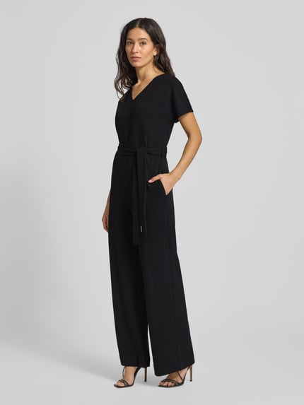 Frauenmodel trägt Jumpsuit mit V-Ausschnitt von Calvin Klein Womenswear aus schwarzem Material-Mix mit Stretch-Anteil, lockerer Schnitt, Taillengürtel, Nahtreißverschluss, Ganzkörperansicht von vorne.