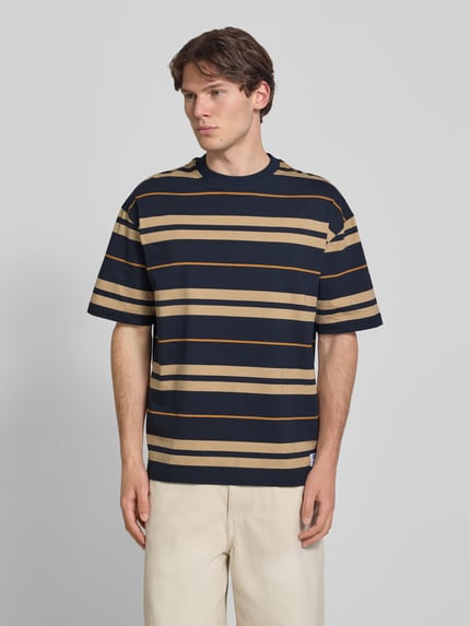 Männermodel trägt Oversized Shirt aus reiner Baumwolle Modell 'NIVARSI' von HUGO in Dunkelblau mit beigefarbenen Streifen, Herren Oversized Shirt von HUGO Blue, Ganzkörperansicht von vorne.