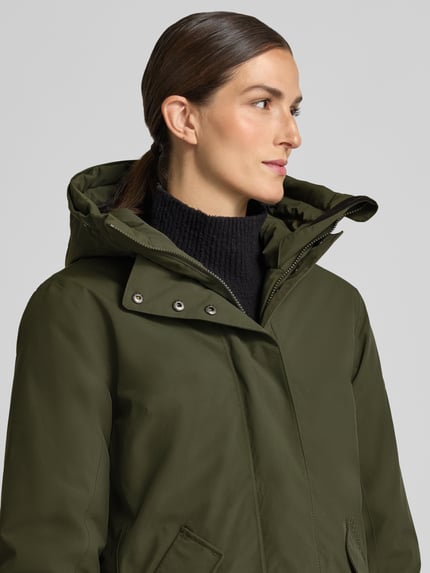 Frauenmodel trägt Regular Fit Parka mit Kunstfellbesatz Modell 'ERNA' von Didriksons in Olivgrün, glatte Textur, Nahaufnahme Oberkörper. Thermore Füllung, 10.000mm Wassersäule, Kapuze, Rückenlänge 93 cm, Schulterbreite 42 cm, Brustweite 51 cm, Ärmellänge 66 cm.