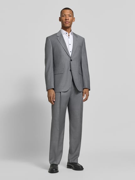 Männermodel trägt Regular Fit Bundfaltenhose aus Wolle von HUGO, grau mit Nadelstreifen, strukturierte Webware, Ganzkörperansicht von vorne.