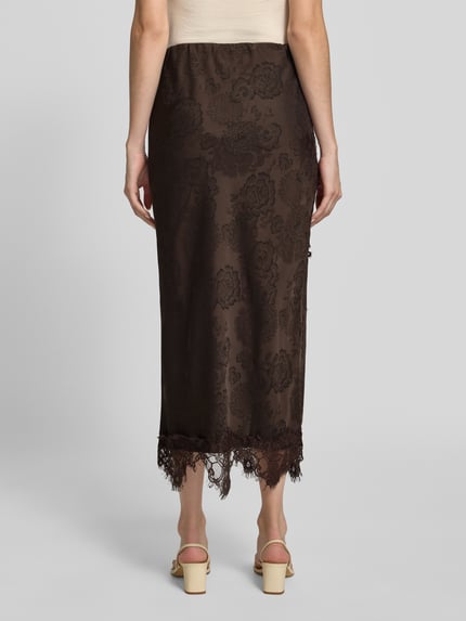 Frauenmodel trägt Midi-Rock mit Spitzenbesatz von VERO MODA in Braun mit floralem Ausbrenner-Effekt und asymmetrischem Saum, Ganzkörperansicht Rückansicht.