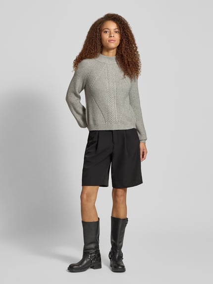 Frauenmodel trägt Regular Fit Strickpullover aus Viskose-Mix Modell 'KATIA' von Only, Zopfmuster, meliert, Mock Neck, Ganzkörperansicht von vorne.