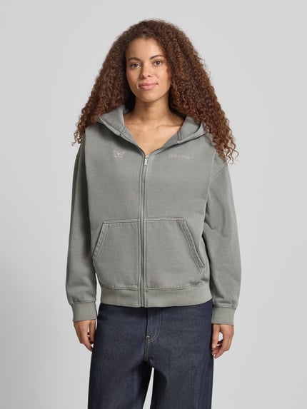 Frauenmodel trägt Oversized Sweatjacke mit Känguru-Tasche Modell 'NIVELLES' von Pegador in Grau, Reißverschluss, Logo, Baumwoll-Mix, Ganzkörperansicht von vorne.