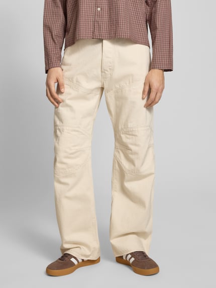 Männermodel trägt Wide Fit Jeans mit achterzakken van G-Star Raw in crème, puur katoen, steekzakken, knoop- en ritssluiting, ganzkörperansicht van voren.