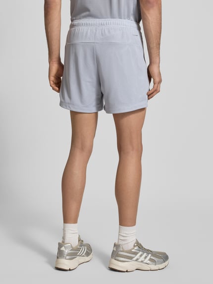 Männermodel trägt Shorts mit Label-Print von adidas Training in Hellgrau mit Lockerer-Schnitt und elastischem Bund, Ganzkörperansicht Rückansicht.
