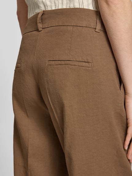 Frauenmodel trägt braune Chino aus Leinen-Mix mit Bügelfalte Modell 'CALIFORNIA' von Cambio, Detailaufnahme Gesäßtaschen, Rückansicht. Damen Chino mit Baumwoll-Anteil, Straight Fit, Haken- und Reißverschluss, französische Eingrifftaschen.