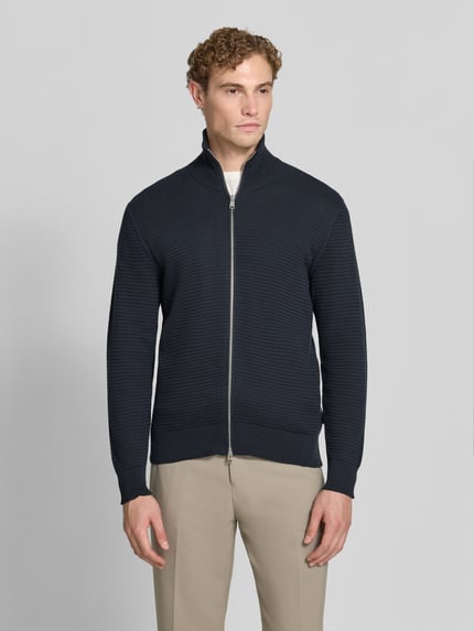 Männermodel trägt Regular Fit Strickjacke aus reiner Baumwolle von Marc O'Polo in Dunkelblau, beige Hose, Ganzkörperansicht von vorne, Herren Pullover von Marc O'Polo.