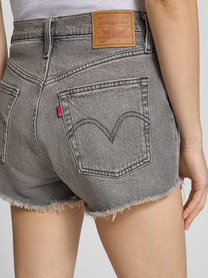 Frauenmodel trägt Regular Fit Jeansshorts aus Baumwoll-Mix Modell '501®' von Levi's®, graues Denim mit Label Patch und Fransen, Nahaufnahme Rückansicht.